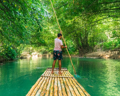 Man rowing bamboo raft along a bright green river in Jamaica